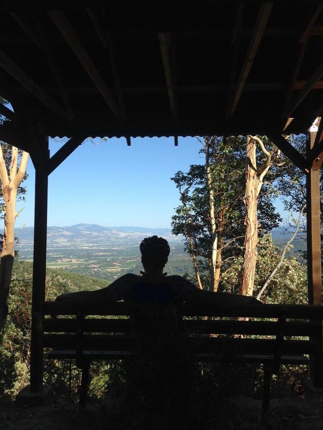 A rider on a bench in a trail shelter on Twin Peaks Trail, looking over the Rogue Valley.