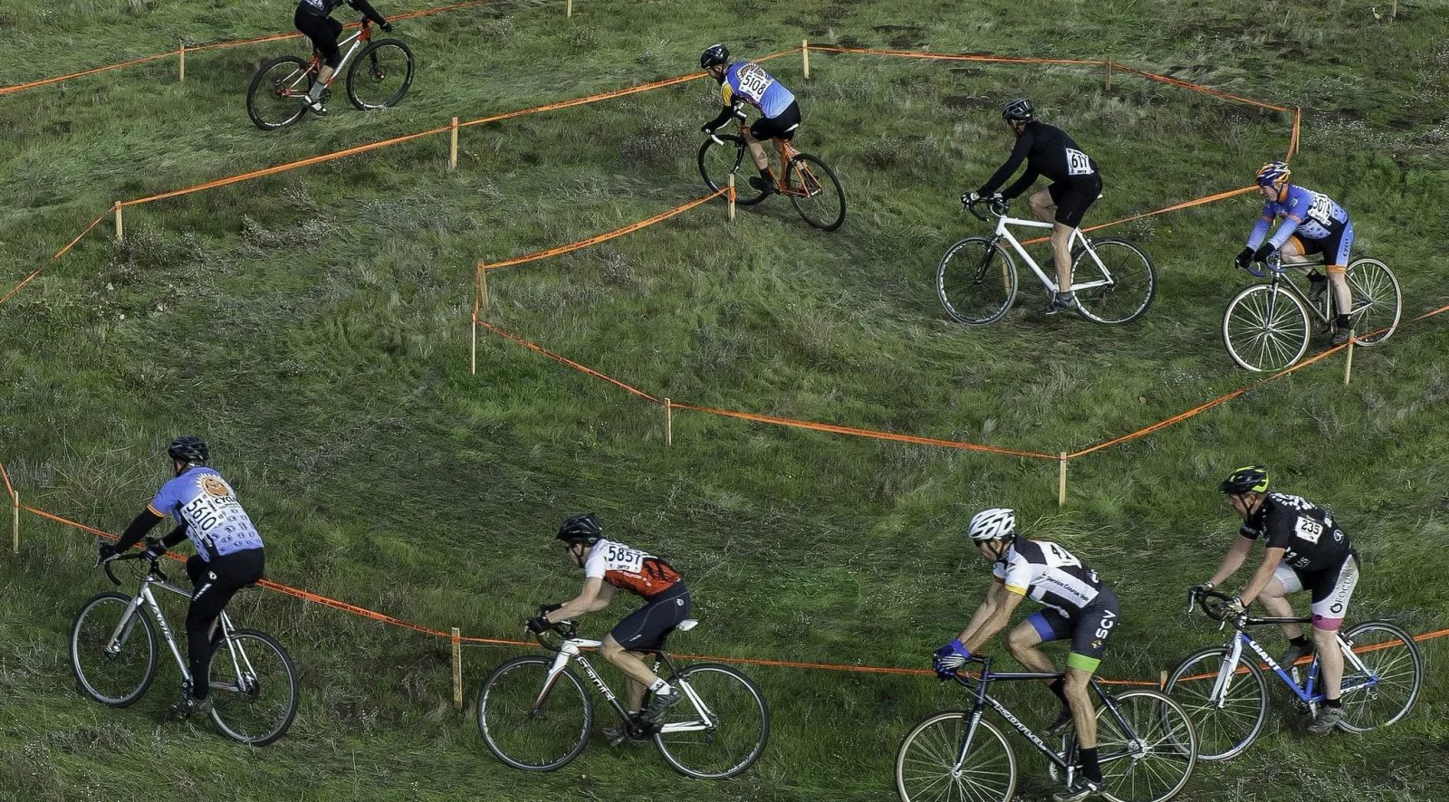 Cyclocross racers strung out across a taped grass course at an Outlaw CX race.