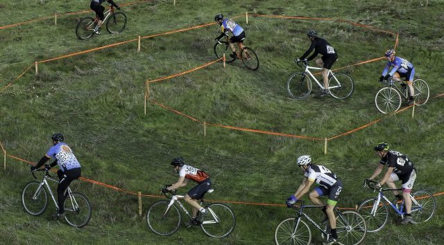 Cyclocross racers strung out across a taped grass course.