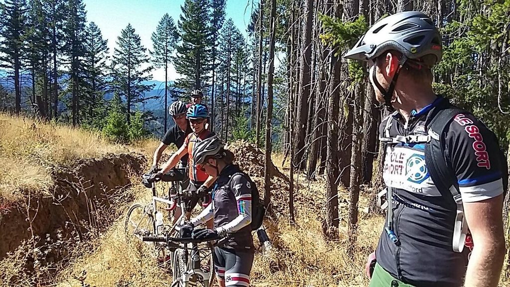 Riders with their bikes stopped beside a dirt track among tall pines on Motorcycle Riders Association land.
